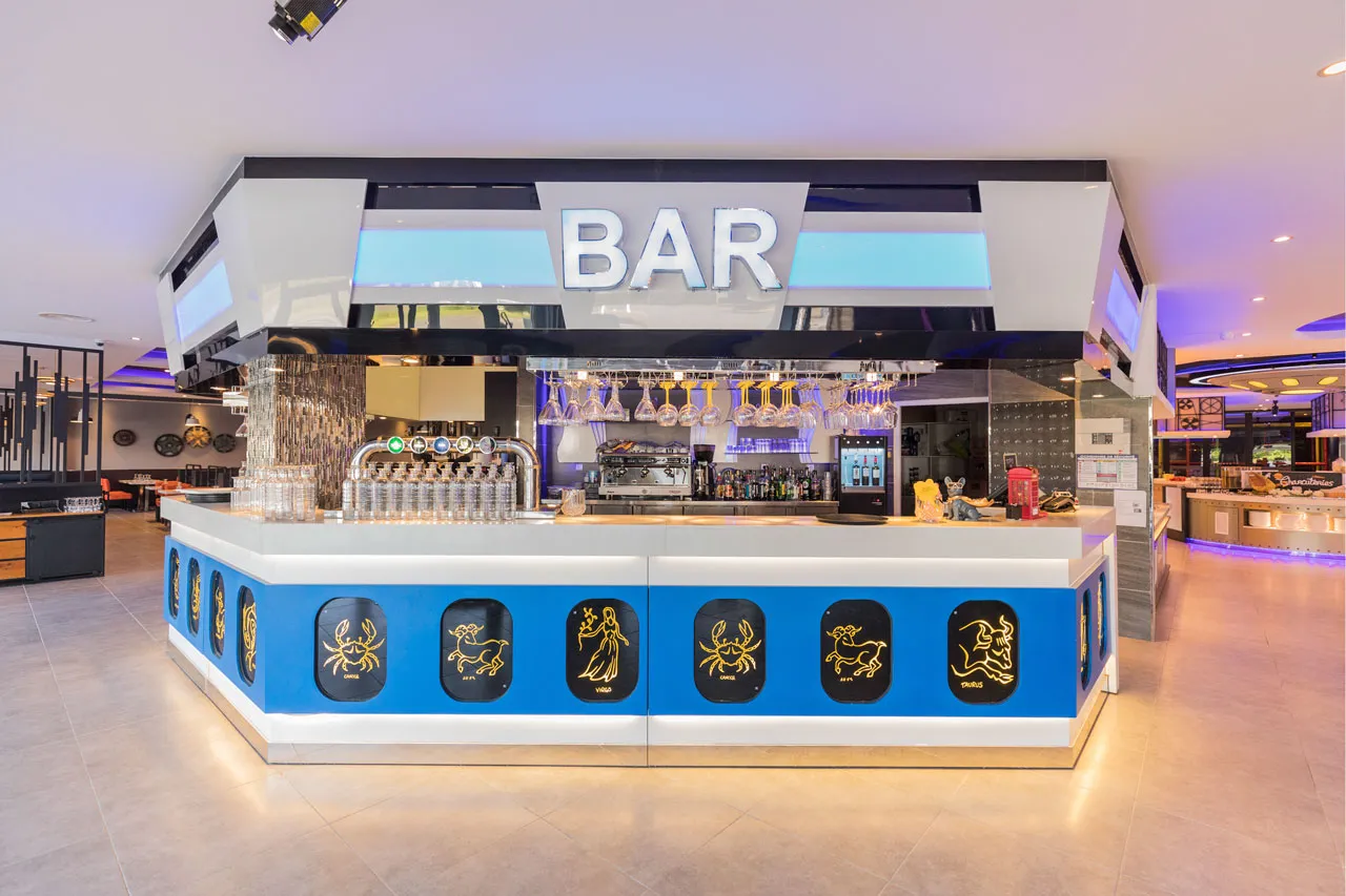 Bar du restaurant avec enseigne lumineuse et panneaux dorés aux signes du zodiaque