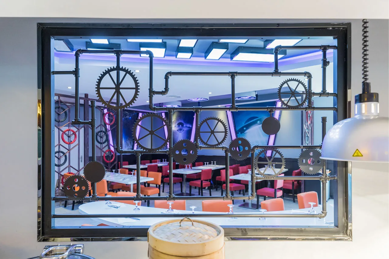 Cloison décorative en tuyaux et engrenages ouvrant sur une salle du restaurant