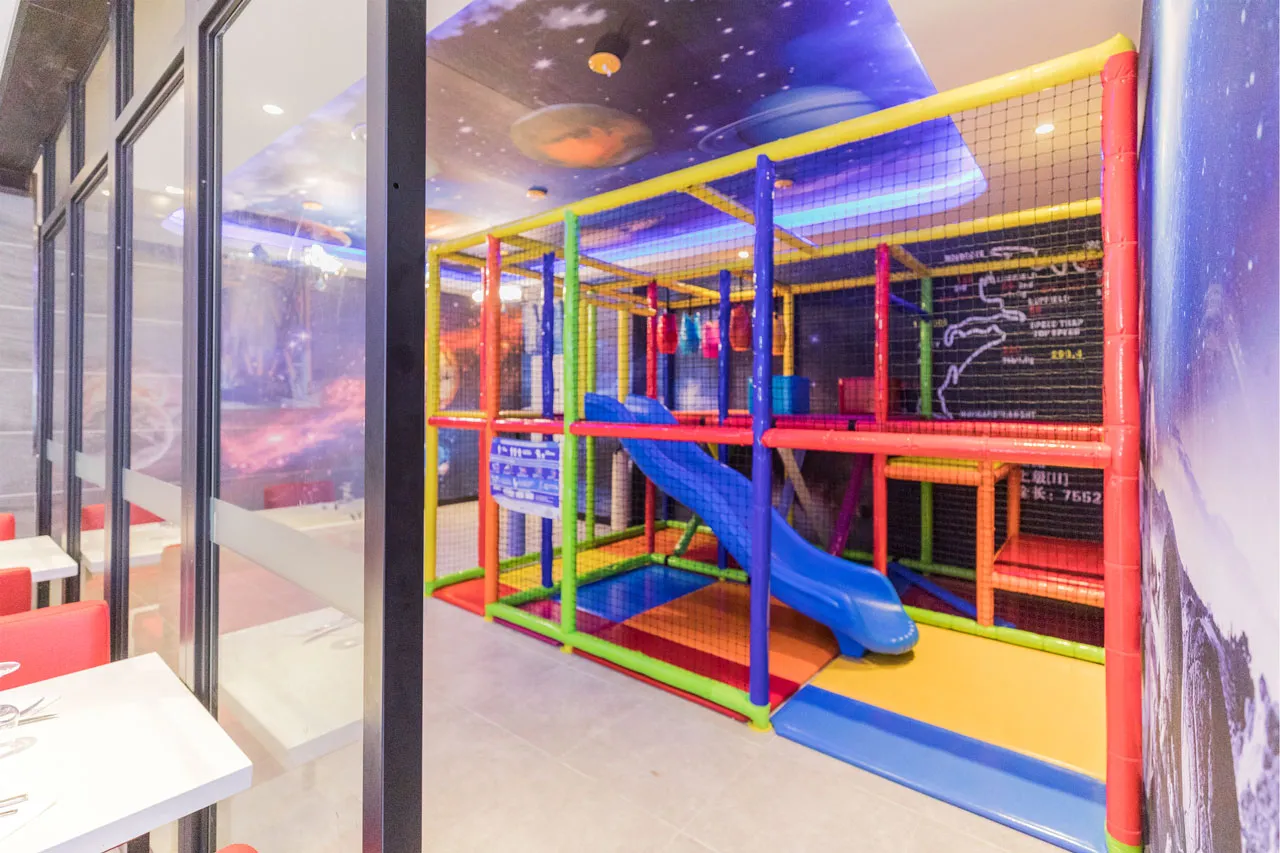 Structure de jeux multicolore vitrée avec toboggan, sous un plafond décoré de planètes