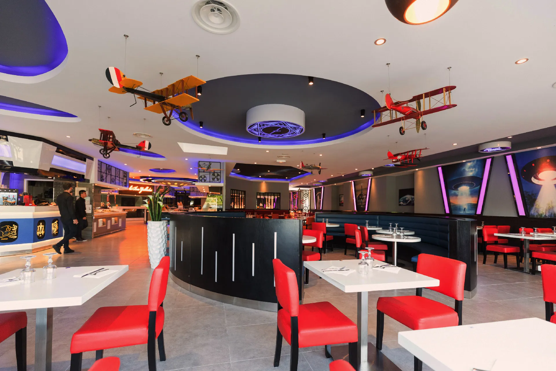 Salle de restaurant avec avions suspendus au plafond et fauteuils rouges