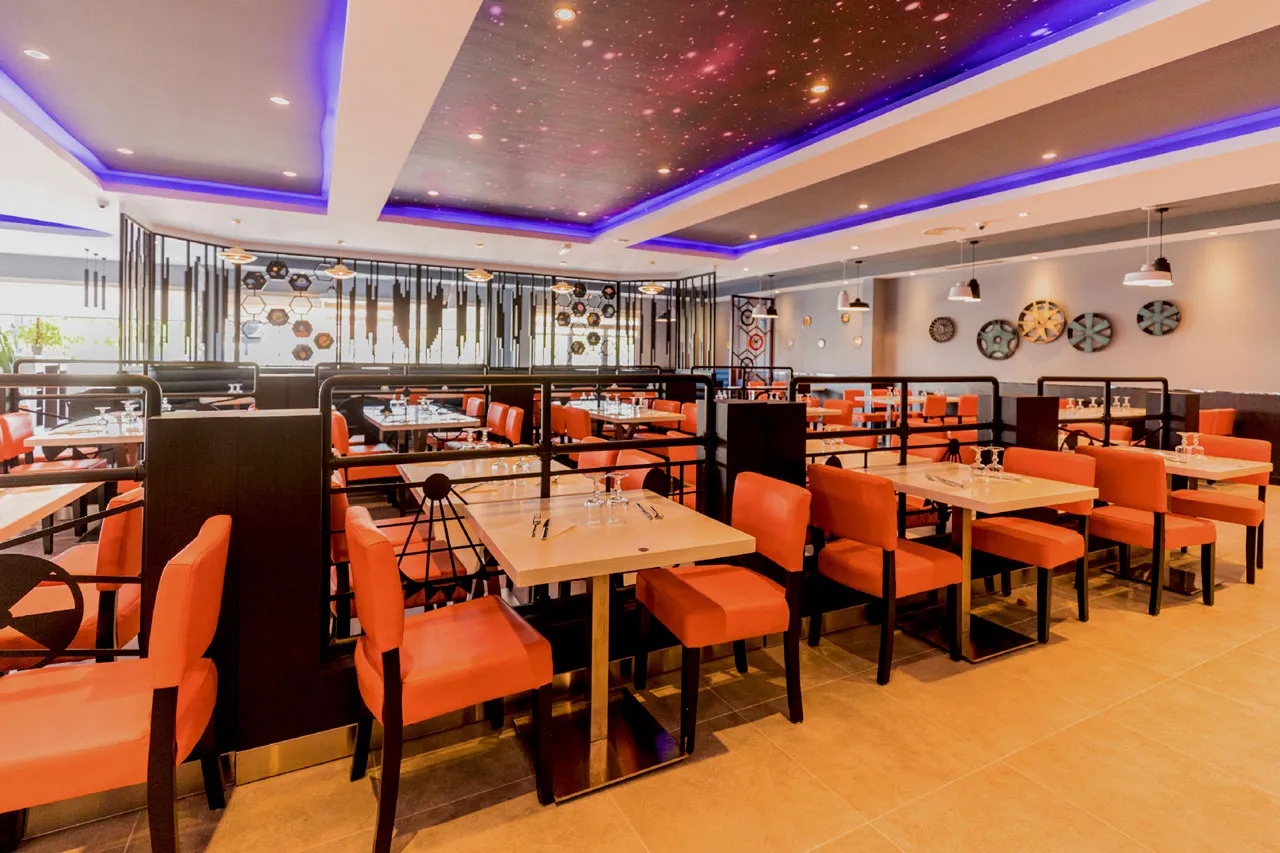 Salle de restaurant avec plafond étoilé rétroéclairé en violet et fauteuils orange