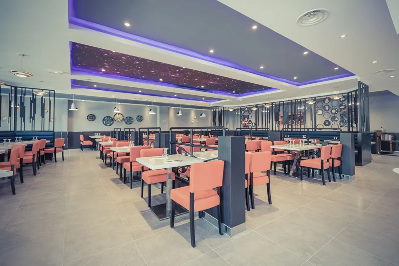 Salle du restaurant dressée pour de grandes tablées sous un plafond étoilé violet